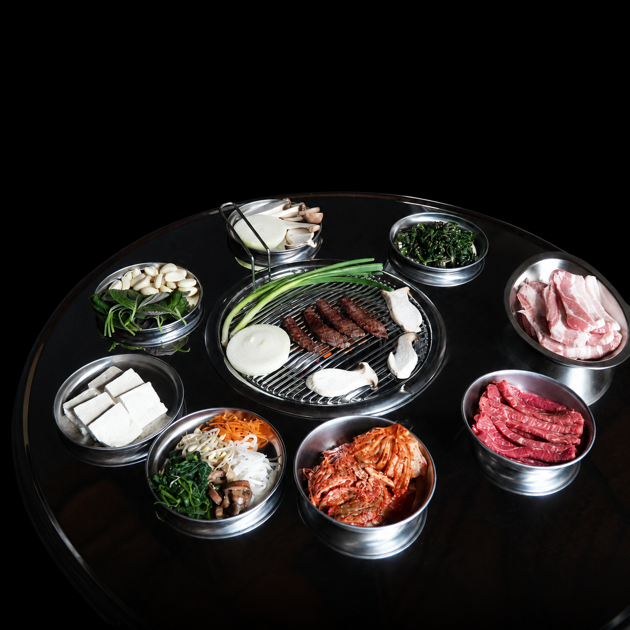 Korean BBQ spread on the round grill table: galbi cooking with raw beef, pork belly and banchan